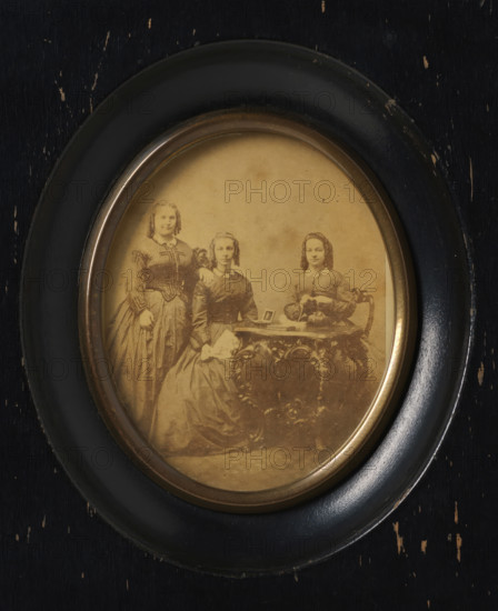 Group portrait of three unknown women around a table, with photos on top, frame, photograph, label:
