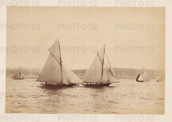 Various sailing ships, including Woodcock and Yvonne, at sea with a hilly landscape in the