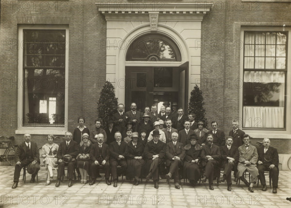Group portrait of men and women in front of the entrance of a building, photograph, stamp: