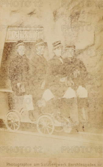 Group portrait of four women wearing caps, sitting on a carriage on a rail, cabinet photograph,