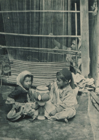 Tunisia, Carpet Manufacturer, Two children playing in front of a woman behind a loom in the