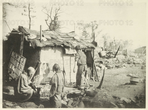 Two women and a man in front of a temporary home in Japan, page, photomechanical print, Japan,