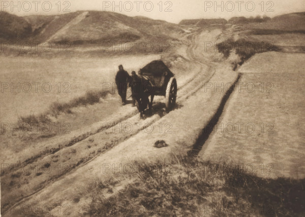 View of two unknown men with a cart on a path through the dunes, The road through the dunes, page,
