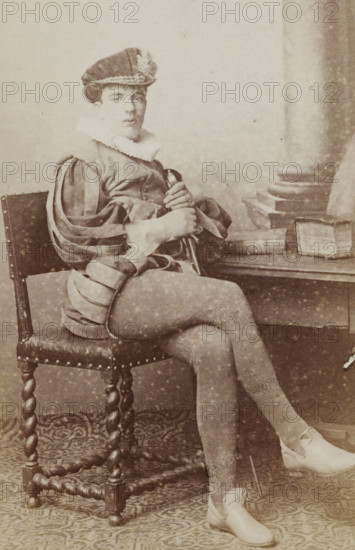 Portrait of a man in a suit sitting at a table with books, identified as J. Wiarda, album page,
