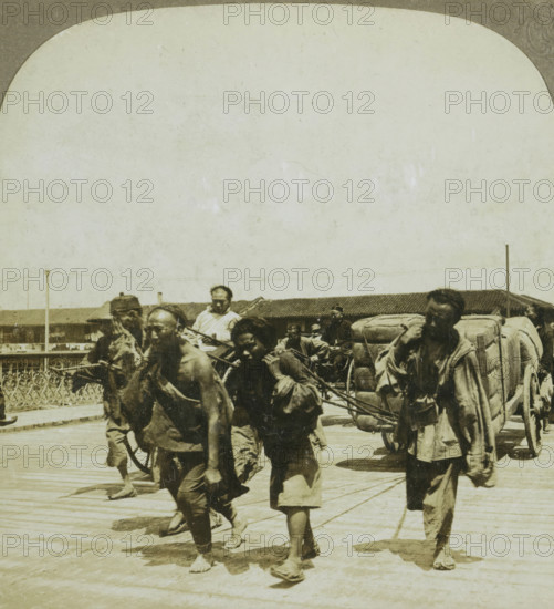 Coolies drawing a heavily loaded truck. Shanghai, China, Four men pulling a heavily loaded cart,