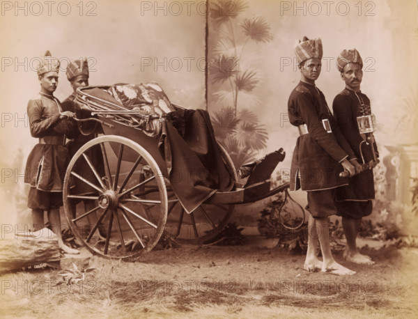 Studio portrait of four Indian men in uniform with a carriage, India, photograph, inscription: