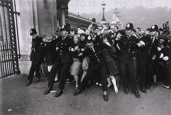 POLICIAS SUJETANDO A LAS FANS DE LOS BEATLES EN EL EXTERIOR DEL PALACIO DE BUCKINGHAM -
