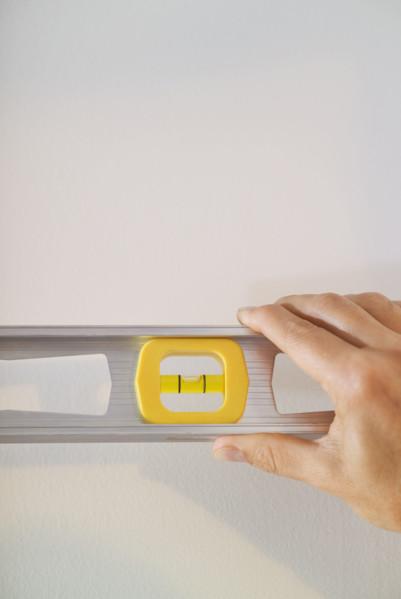 Hand holding a level against a wall.