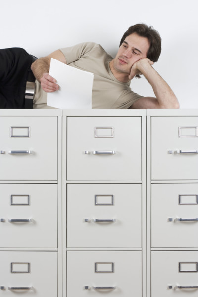 Man reading lying atop file cabinets.