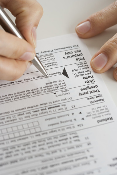 Closeup of hands signing tax form.