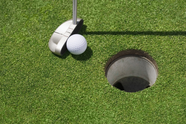 Golf ball near cup on putting green outdoors.