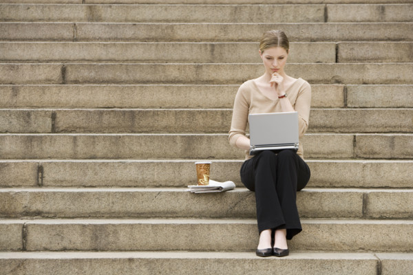 Young woman sitting outdoors on stairs with laptop.