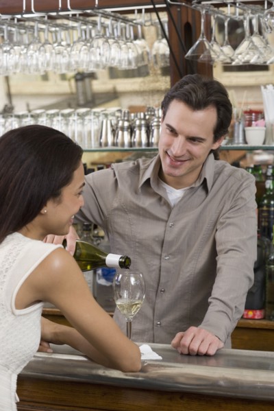 Male bartender pouring wine for female customer.