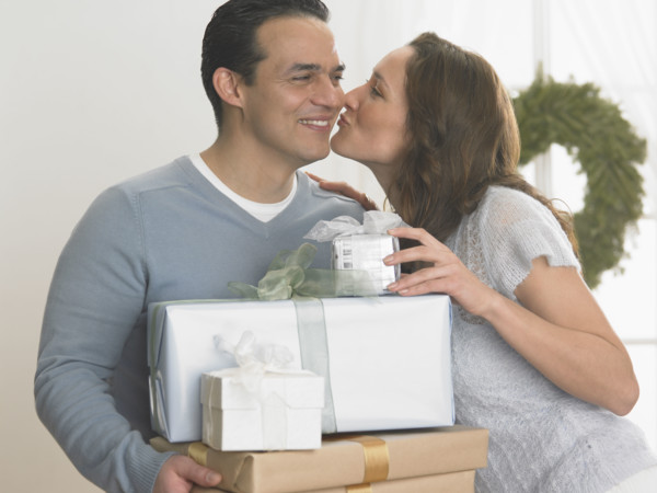 Woman kissing man holding Christmas gifts.