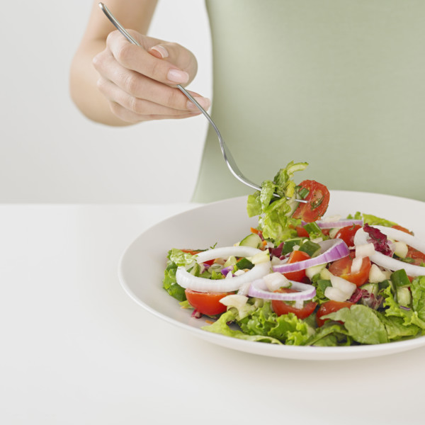 Close up of woman eating plate of salad.