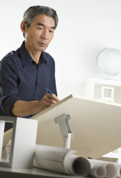 Asian businessman at drafting table with blueprints.