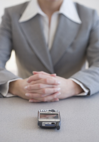 Businesswoman with hands clasped next to cell phone.