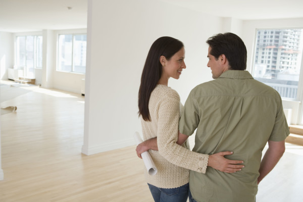 Couple hugging and holding blueprints in empty house.