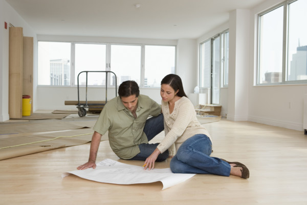 Couple looking at blueprints on floor in new house.