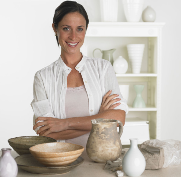 Female potter smiling next to pottery.