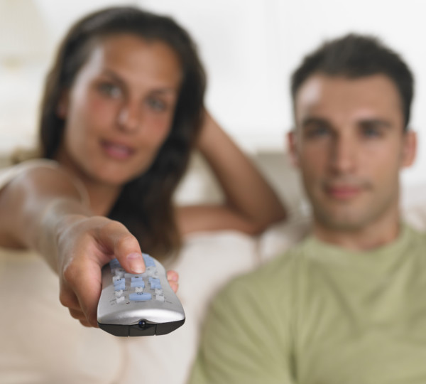 Couple sitting on sofa pointing remote control.