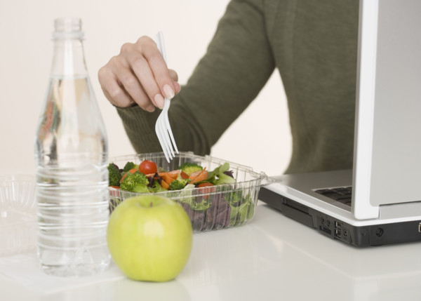 Woman eating salad next to laptop.