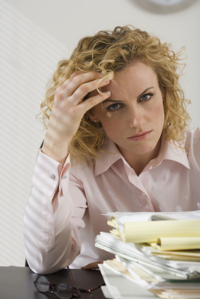 Businesswoman rubbing temple and looking at paperwork.