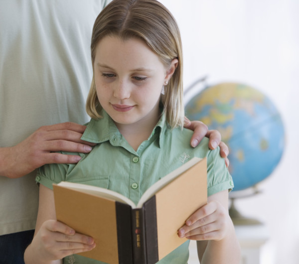 Girl reading book next to father.