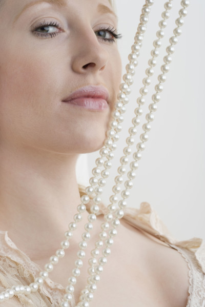 Woman with pearl necklace against face.