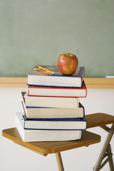 Stack of books and apple in classroom.