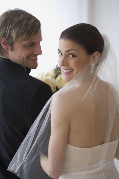 Portrait of bride and groom looking over shoulders.