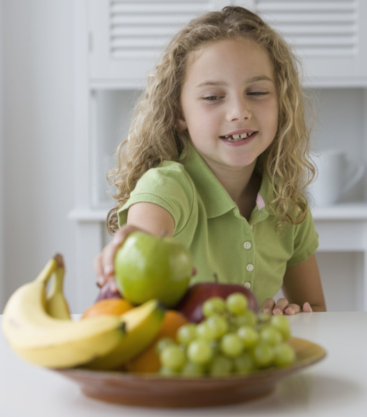 Girl reaching for fruit in bowl.