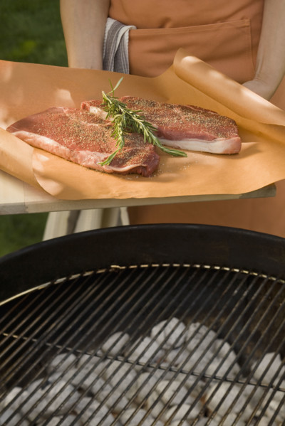 Person holding steaks next to grill.