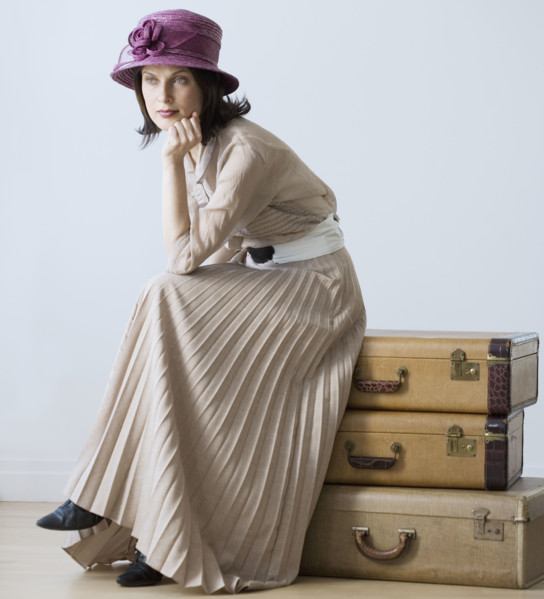 Woman in vintage clothing sitting on suitcases.
