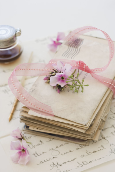 Stack of old letters next to flowers and ink bottle.