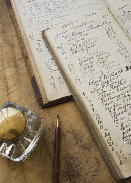 Quill pen and ink jar next to old ledger books.