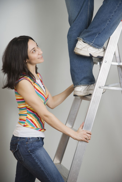 Woman holding ladder while man climbs. Date : 2006