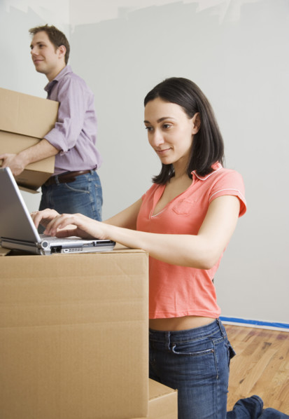 Woman using laptop while man carries box in new house. Date : 2006