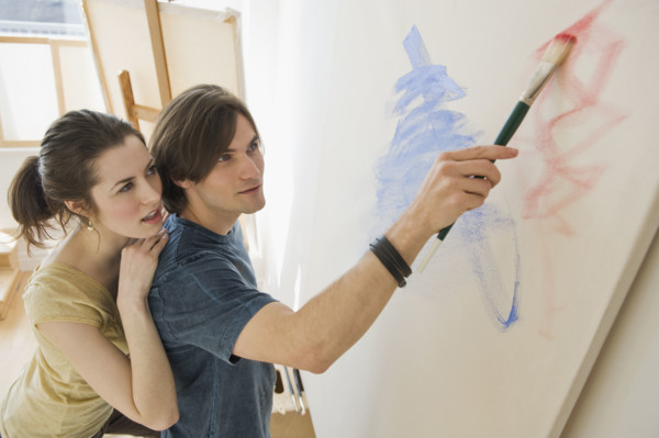 Woman watching boyfriend paint on easel.