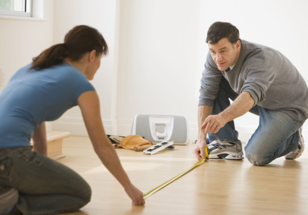 Couple measuring floor with tape measure.