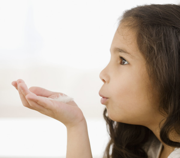 Hispanic girl blowing on feather in hand. Date : 2008