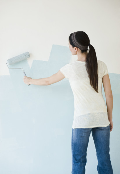 Woman painting wall with paint roller.