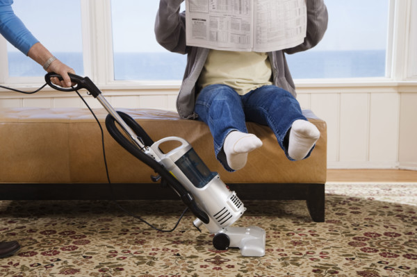 Woman vacuuming under man’s feet. Date : 2008