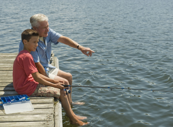 Grandfather and grandson fishing off dock.