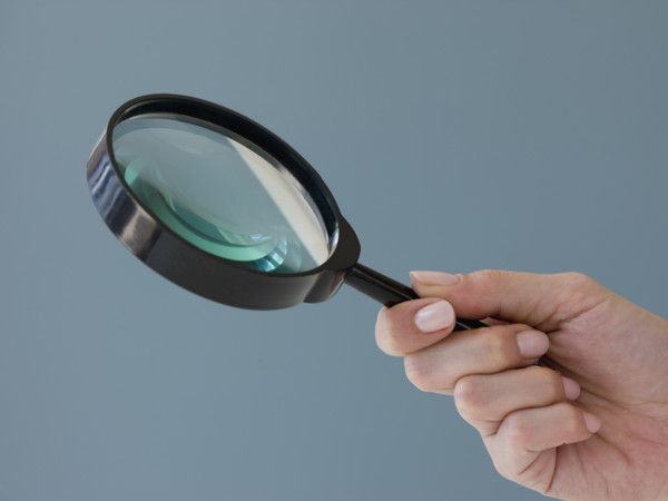 Close up of hand holding magnifying glass.