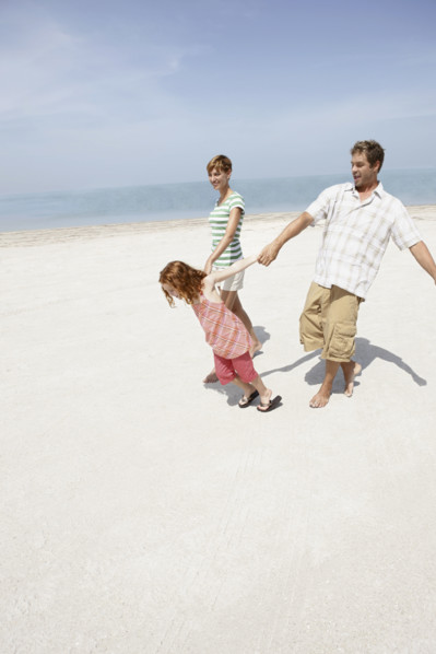 Girl holding hands with mother and father on beach. Date : 2008