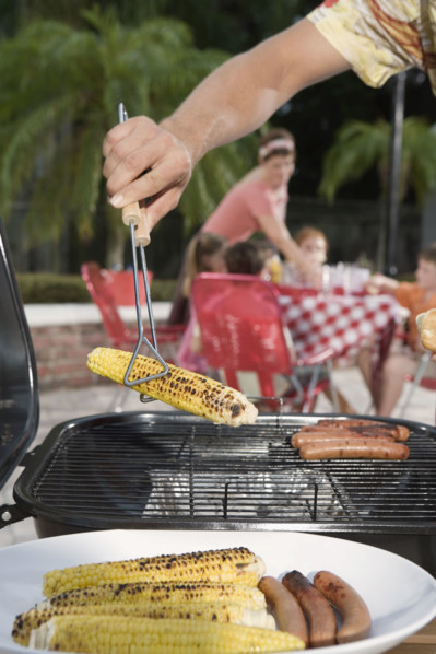 Man grilling hotdogs and corn in backyard. Date : 2008