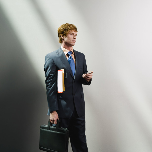 Businessman holding cell phone, files and briefcase. Date : 2008