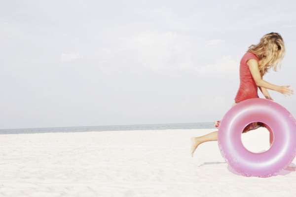 Teenage girl rolling inflatable ring on beach. Date : 2008