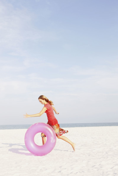 Teenage girl rolling inflatable ring on beach. Date : 2008